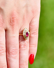 Load image into Gallery viewer, Close up of hand wearing a ring with a ruby surrounded by diamonds against a blurred green background