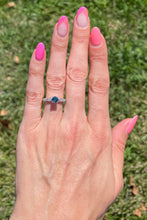 Load image into Gallery viewer, Vintage platinum ring set in the center with a color enhanced fancy blue round diamond, with white diamond side stones modeled on a hand.