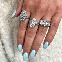Load image into Gallery viewer, Hand wearing three vintage diamond rings on a textured beige background