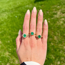 Load image into Gallery viewer, Hand wearing three emerald and diamond rings with a green background