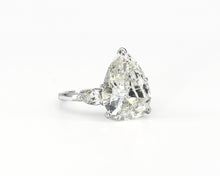 Load image into Gallery viewer, Side view of a platinum three-stone engagement ring featuring a  7.63CT pear-shaped diamond centered between two smaller pear-shaped diamonds.
