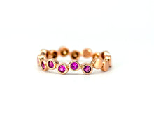 Load image into Gallery viewer, A product photo side view of 14K rose gold stackable band bezel set round pink sapphires alternating between top and bottom positions to form a staggered pattern on a plain white backdrop.
