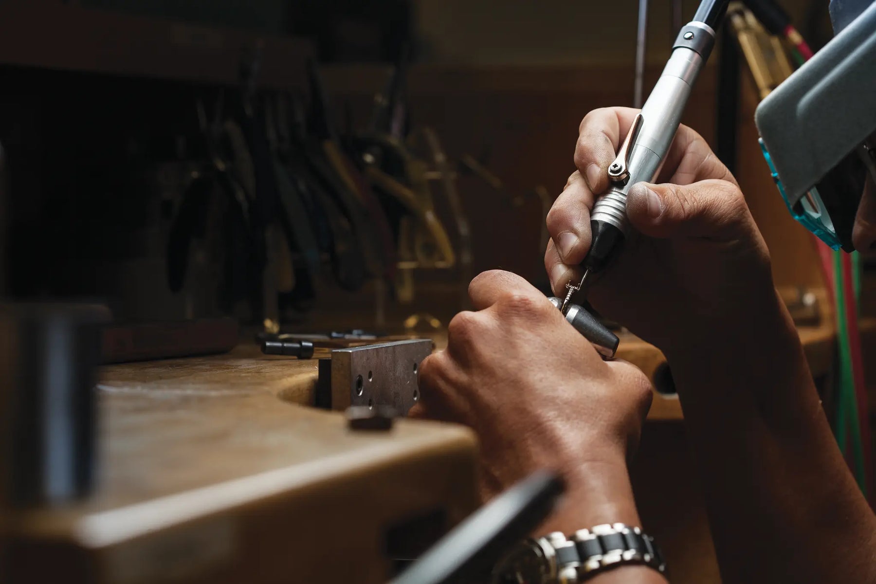 Close-up of a jewelers' hands using a tool on a wooden workbench with tools in the background