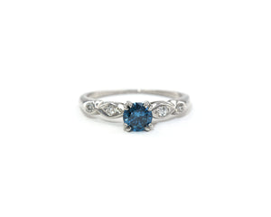 Vintage platinum ring set in the center with a color enhanced fancy blue round diamond, with white diamond side stones.