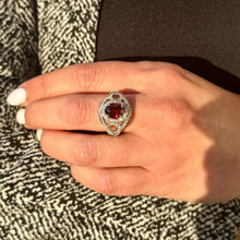 Load image into Gallery viewer, Hand wearing a Rhodolite Garnet and Diamond Ring on a textured fabric background
