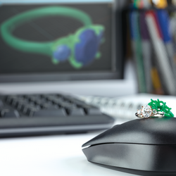 Mouse with a ring and a wax model of a ring on top in front of a computer setup showing CADCAM custom jewelry design of a ring.