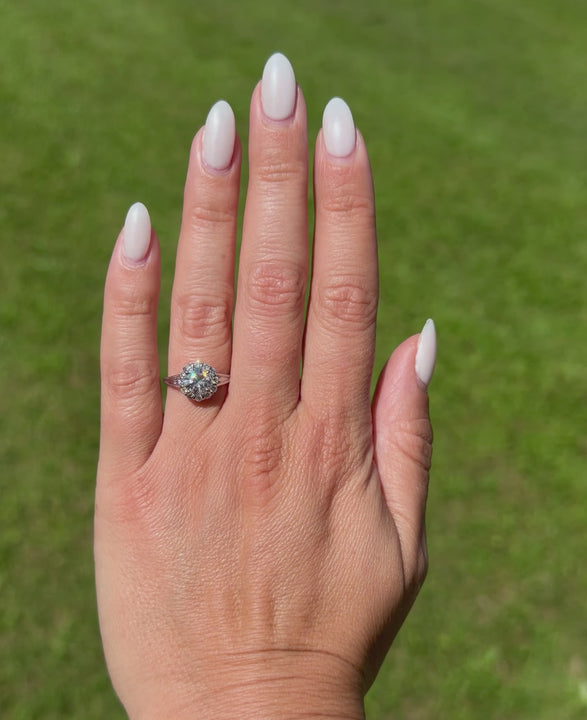 Video of a hand wearing a signed Verragio 14K white gold engagement ring featuring a round brilliant-cut center diamond, halo setting, and split shank, filmed outdoors against a blurred green lawn background.